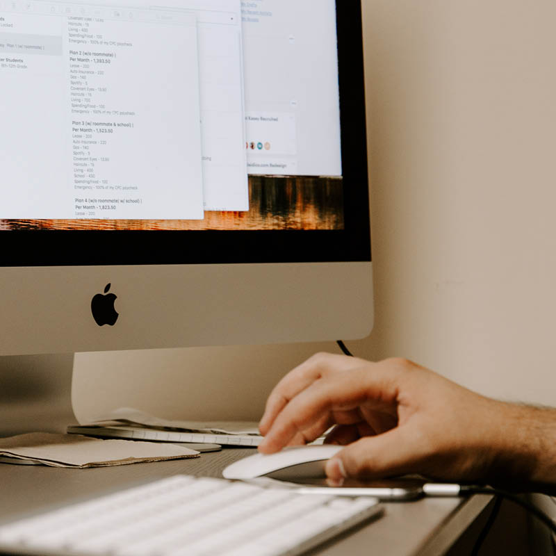 Hand on mouse beside Apple monitor